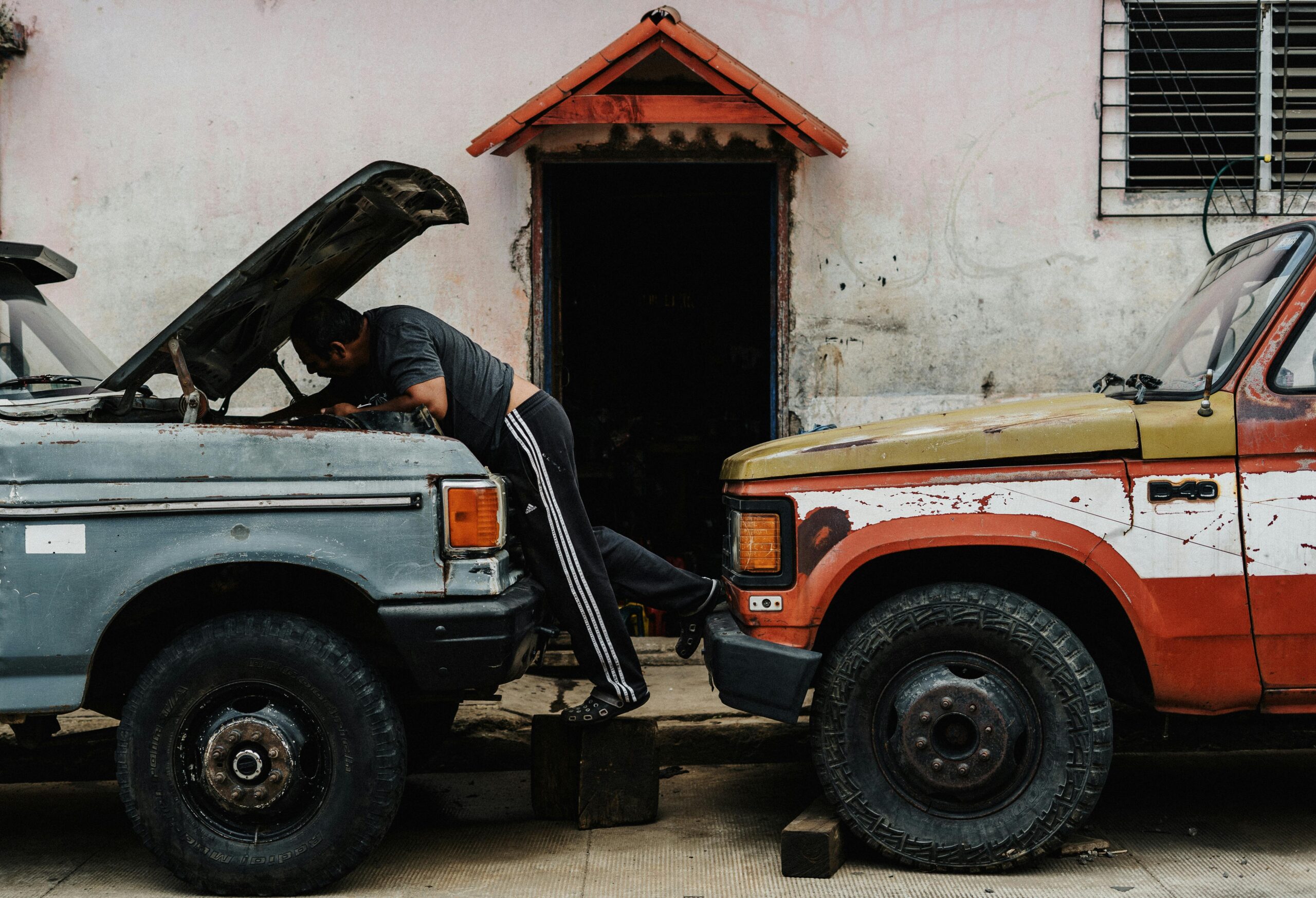 Mechanic working on vintage trucks in an urban setting, highlighting a candid street scene.